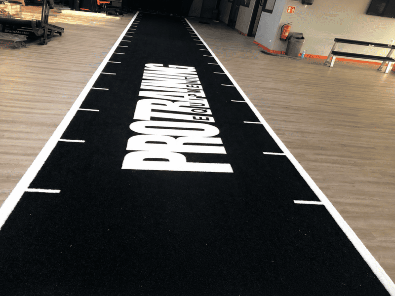 Professional flooring installer applying heavy duty adhesive to lay an SPU backed gym turf roll flat